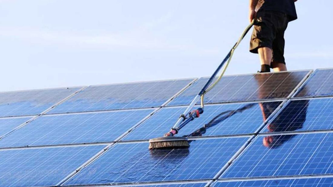 Technician soft-washing a residential solar panel array